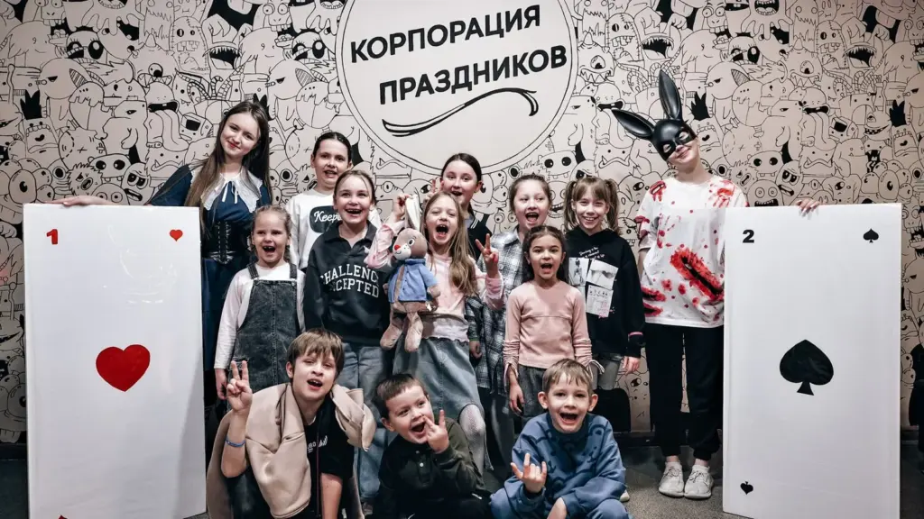 Участники квеста «Алиса в стране кошмаров» и ведущие в образах героев у стены с логотипом